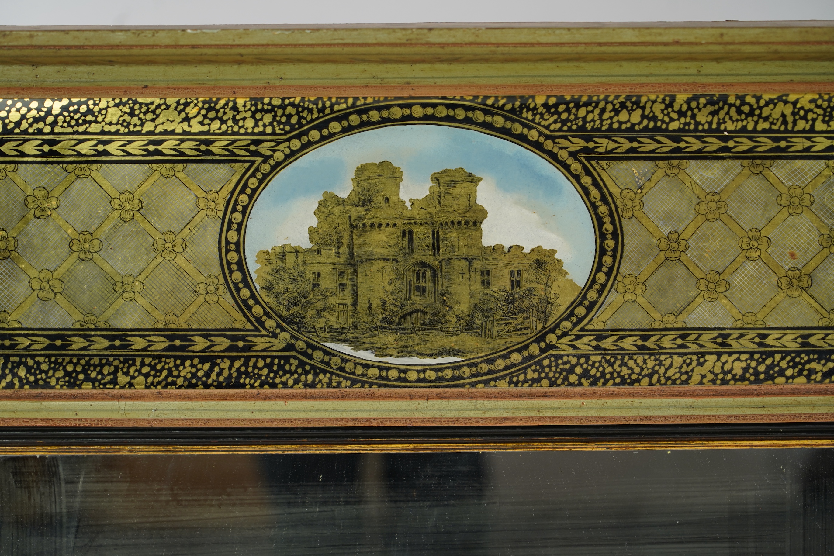 A Regency giltwood and composition overmantel mirror, with verre eglomise tablet frieze depicting a castle facade over a rectangular plate with reeded ebonised slip flanked by turned floral painted projecting columns, wi
